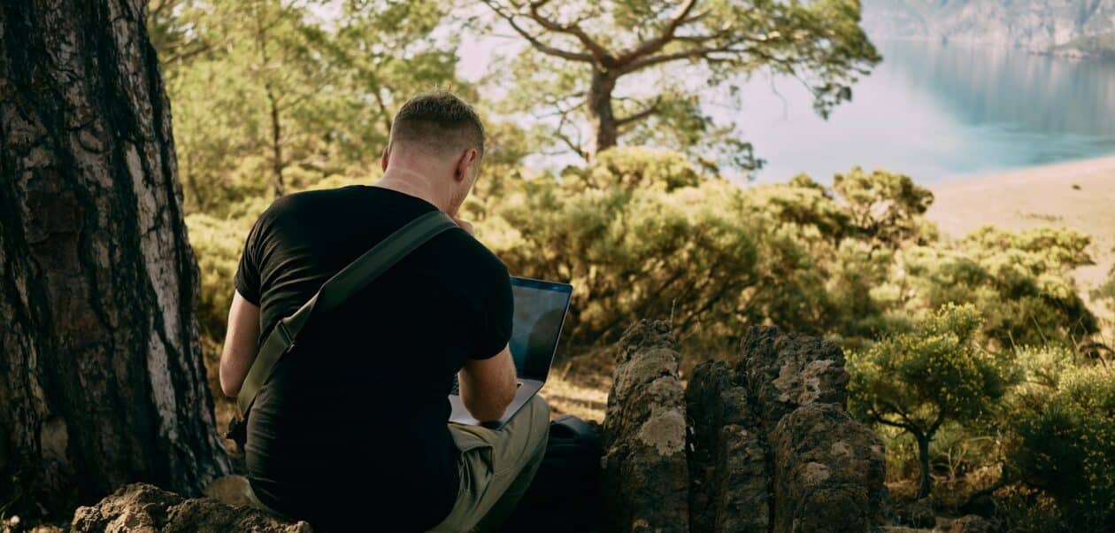 10 Non-Negotiable Apps for Workation in India A digital nomad working on a laptop in a remote nature setting, representing the importance of essential apps for workation in India.