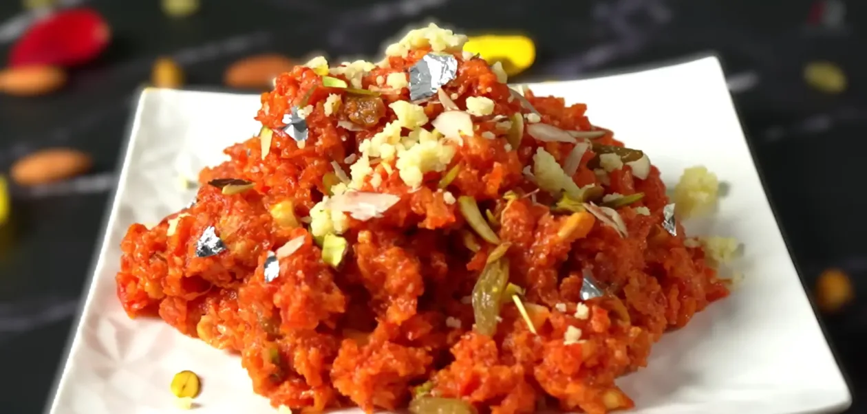 Gajar Ka Halwa served on a white plate, one of the most beloved Indian Comfort Dishes for winter, made from seasonal red carrots and garnished with nuts and silver leaf.
