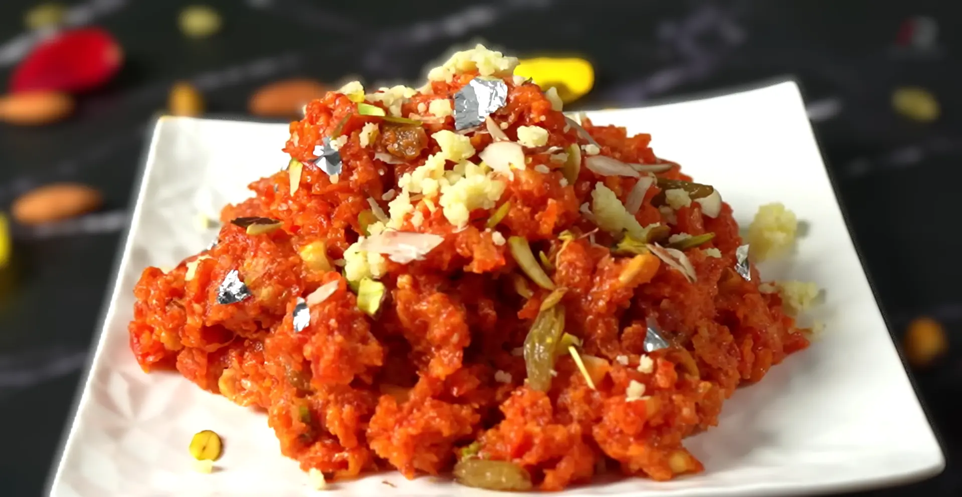 Gajar Ka Halwa served on a white plate, one of the most beloved Indian Comfort Dishes for winter, made from seasonal red carrots and garnished with nuts and silver leaf.