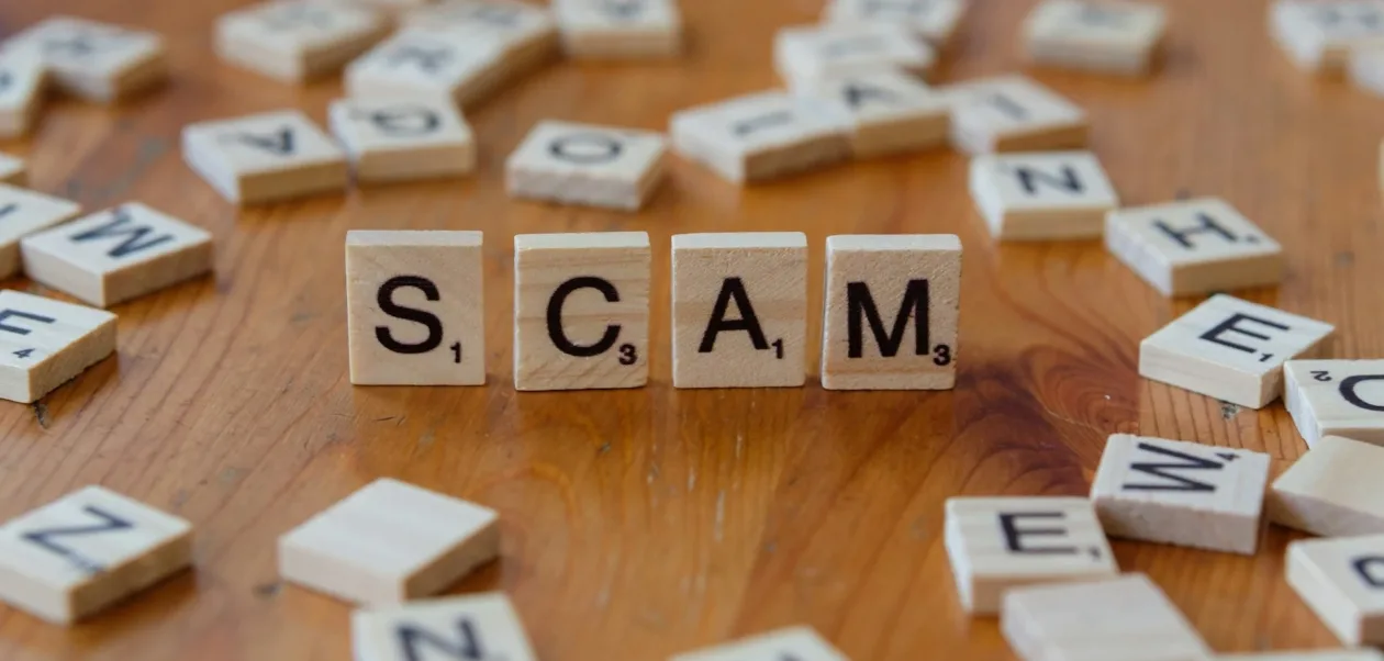 AI Refund Scams: Scrabble tiles on a wooden table spelling out the word "SCAM." Illustrates the intentional and costly nature of AI Refund Scams in quick commerce.